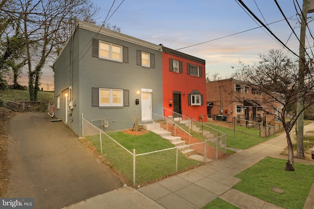 view of front of home featuring a lawn, entry steps, aphalt driveway, a fenced front yard, and brick siding