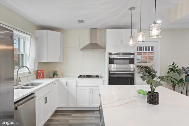 kitchen with visible vents, a sink, white cabinets, appliances with stainless steel finishes, and wall chimney exhaust hood