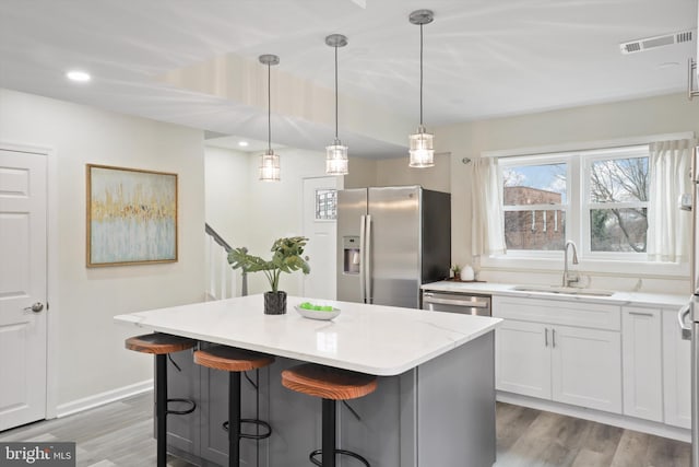 kitchen featuring visible vents, a kitchen island, light wood-style flooring, a sink, and appliances with stainless steel finishes