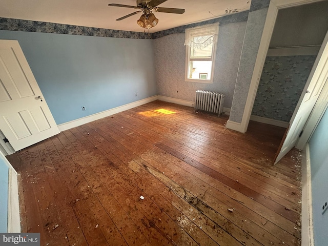 unfurnished bedroom featuring baseboards, wallpapered walls, radiator heating unit, ceiling fan, and hardwood / wood-style flooring