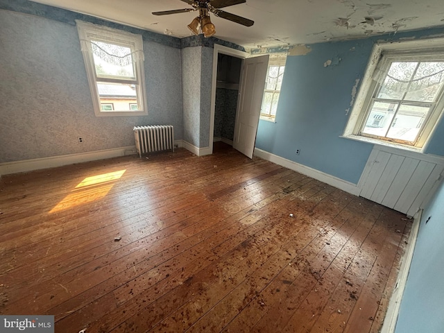 unfurnished bedroom featuring wallpapered walls, baseboards, radiator, and hardwood / wood-style flooring