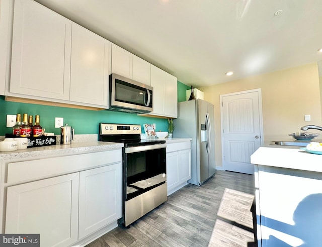 kitchen with light wood finished floors, a sink, stainless steel appliances, light countertops, and white cabinetry