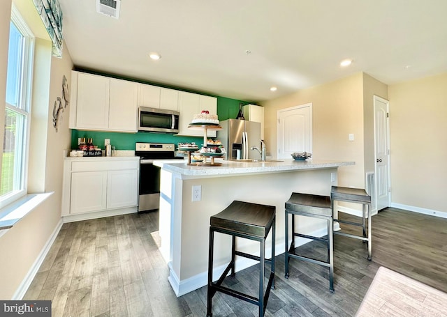 kitchen with visible vents, light wood finished floors, an island with sink, stainless steel appliances, and white cabinets