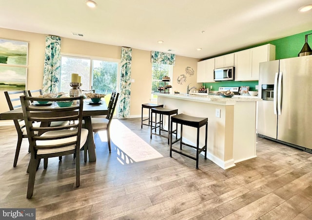 kitchen with light wood finished floors, recessed lighting, a kitchen island with sink, appliances with stainless steel finishes, and white cabinetry