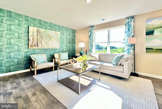 living room with wood finished floors, visible vents, baseboards, wallpapered walls, and an accent wall