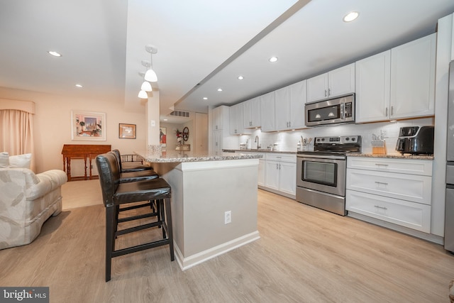 kitchen featuring a breakfast bar area, light stone counters, stainless steel appliances, light wood-style floors, and white cabinetry