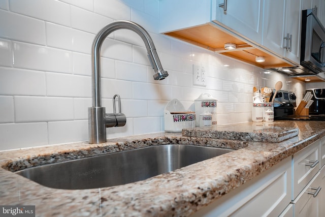 interior details featuring decorative backsplash, light stone counters, stainless steel appliances, and a sink