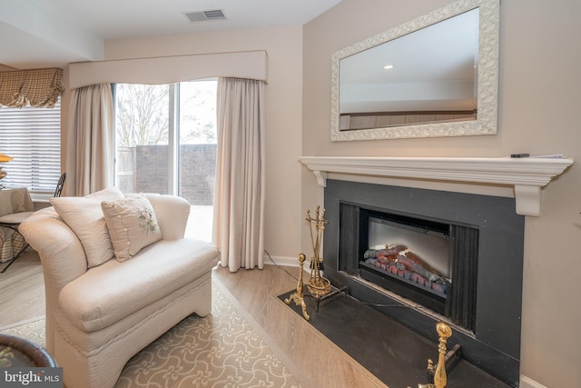 living room with visible vents, a healthy amount of sunlight, a fireplace with flush hearth, and wood finished floors