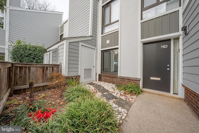 doorway to property featuring brick siding and fence