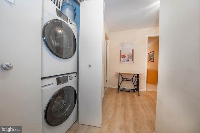 clothes washing area with laundry area, stacked washer and clothes dryer, baseboards, and light wood-style floors