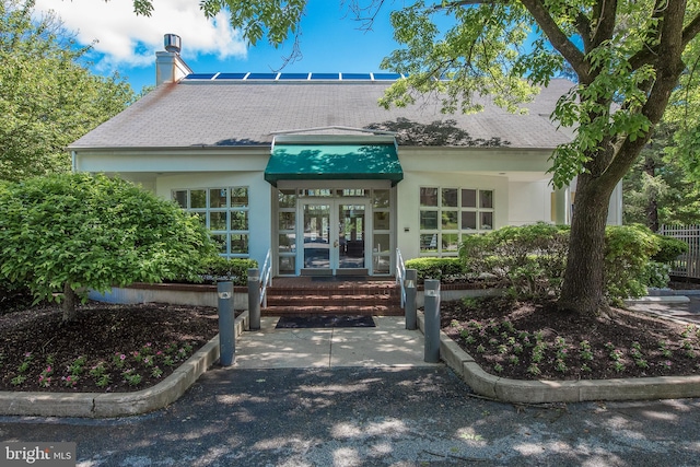 exterior space featuring stucco siding, french doors, roof with shingles, and a chimney