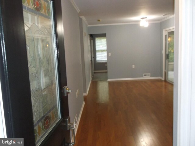 hallway with baseboards, wood finished floors, visible vents, and ornamental molding