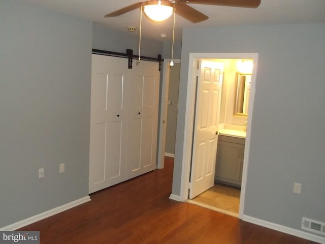 unfurnished bedroom featuring visible vents, connected bathroom, baseboards, a barn door, and wood finished floors