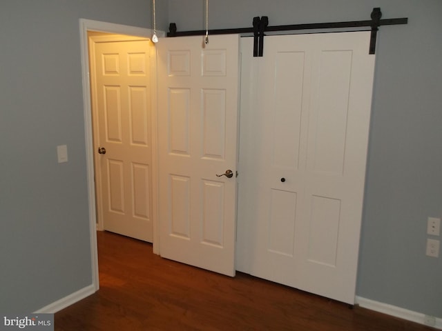 interior space with a barn door, baseboards, and dark wood-type flooring