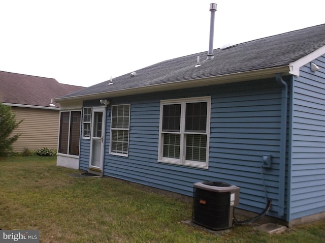 rear view of house with a yard, central air condition unit, and a shingled roof