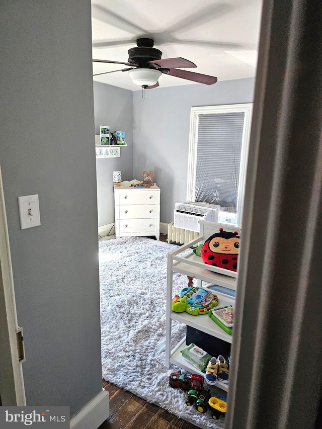 bedroom featuring a nursery area, a ceiling fan, and wood finished floors