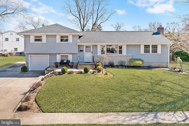 split level home featuring roof with shingles, a chimney, a front lawn, concrete driveway, and a garage