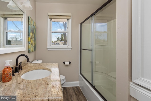 full bath featuring toilet, wood finished floors, shower / bath combination with glass door, baseboards, and vanity