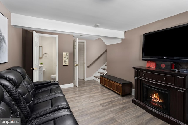 living room featuring stairs, light wood-style flooring, baseboards, and a lit fireplace