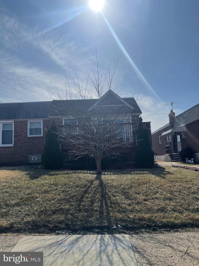 rear view of property with a yard, brick siding, and roof with shingles