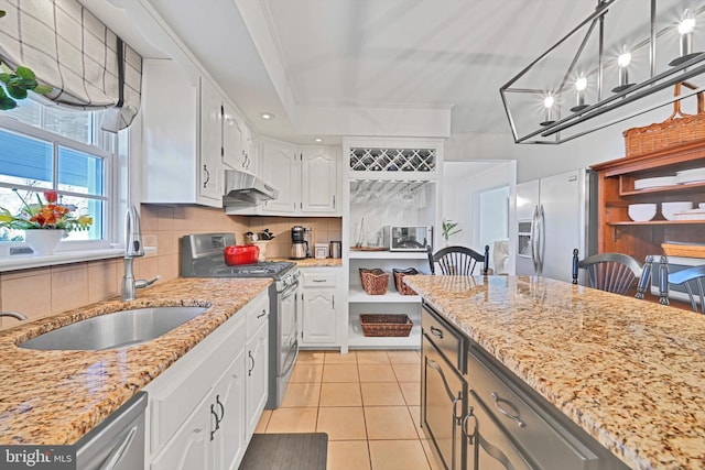 kitchen with a sink, under cabinet range hood, appliances with stainless steel finishes, white cabinetry, and backsplash