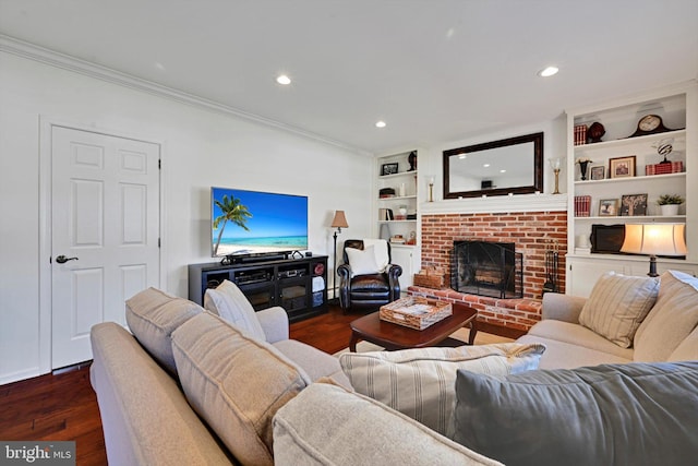 living room with built in shelves, recessed lighting, dark wood-style flooring, crown molding, and a brick fireplace