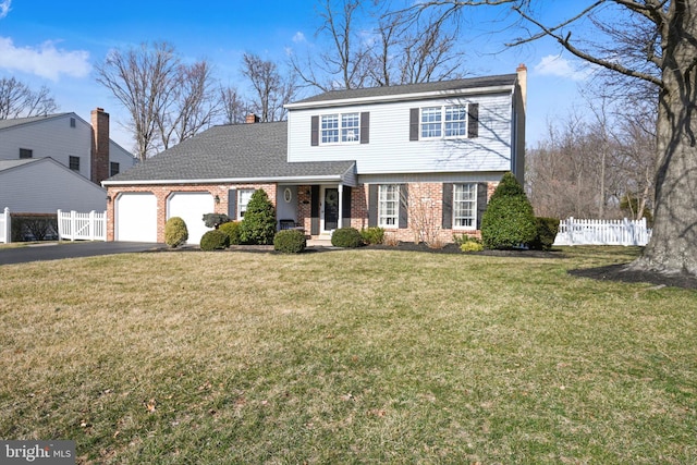 colonial house featuring brick siding, fence, a front yard, a garage, and driveway