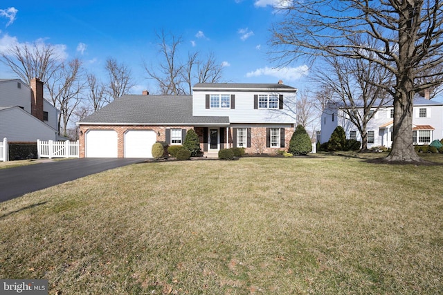 colonial-style house with fence, a front lawn, a garage, aphalt driveway, and brick siding