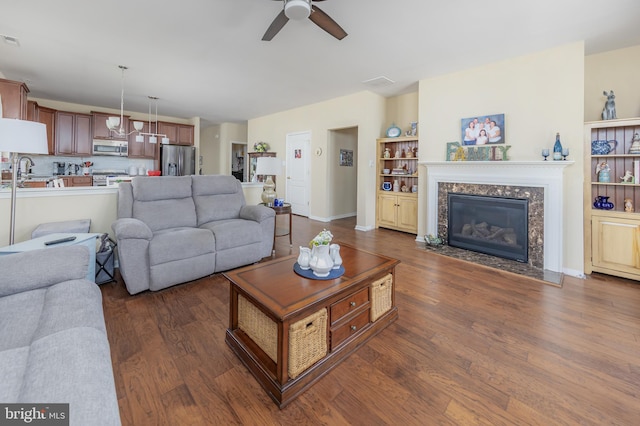 living area with a high end fireplace, visible vents, baseboards, dark wood-style floors, and a ceiling fan