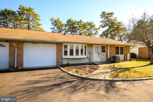 ranch-style house with cooling unit, brick siding, an attached garage, and aphalt driveway