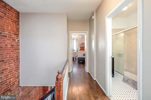 hallway with dark wood finished floors, brick wall, and baseboards