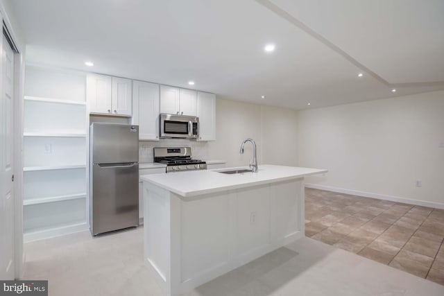 kitchen featuring an island with sink, a sink, tasteful backsplash, stainless steel appliances, and white cabinets