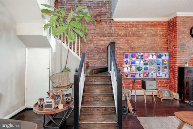 stairway with wood finished floors, brick wall, and ornamental molding