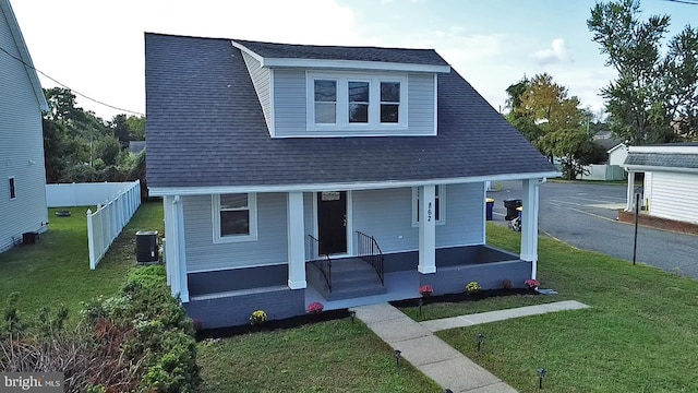 bungalow-style home featuring a shingled roof, fence, a porch, a front yard, and central AC unit