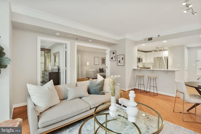 living room featuring visible vents, light wood-type flooring, baseboards, and ornamental molding