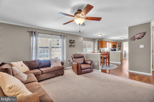 living area with baseboards, light carpet, ceiling fan, and crown molding