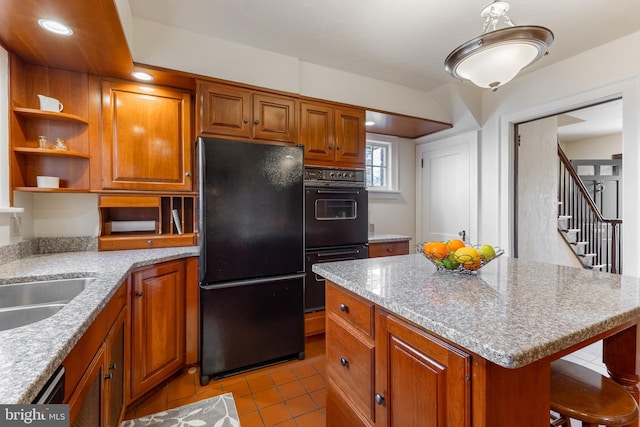 kitchen featuring light tile patterned floors, brown cabinetry, a kitchen island, a sink, and black appliances