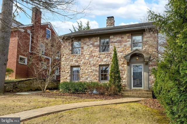 view of front of property featuring a front lawn, stone siding, and a chimney