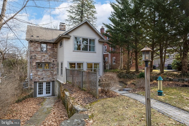 view of front of house with fence, roof with shingles, french doors, a chimney, and stone siding