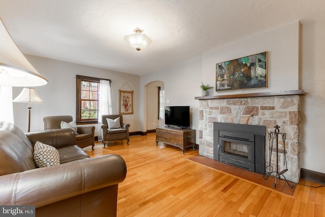 living room with baseboards, hardwood / wood-style floors, a fireplace, arched walkways, and a textured ceiling