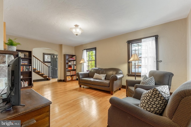 living area with baseboards, stairs, light wood-type flooring, arched walkways, and a textured ceiling