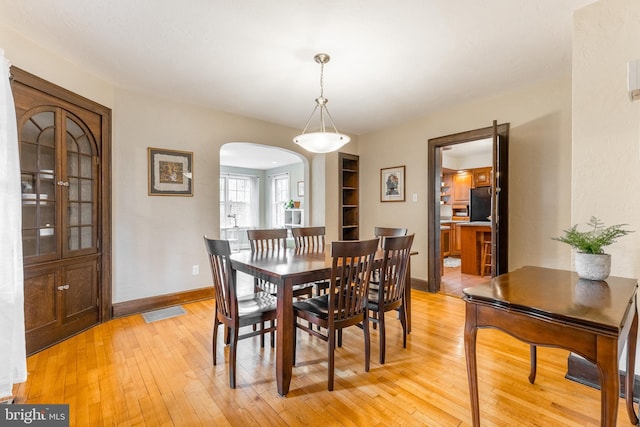 dining area with light wood-type flooring, arched walkways, baseboards, and visible vents