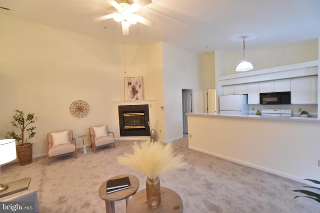 living area featuring baseboards, light carpet, a high ceiling, a glass covered fireplace, and a ceiling fan