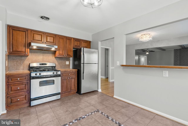 kitchen with under cabinet range hood, brown cabinets, stainless steel appliances, and tasteful backsplash