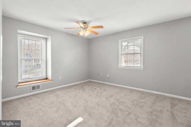 empty room featuring plenty of natural light, a ceiling fan, visible vents, and carpet floors