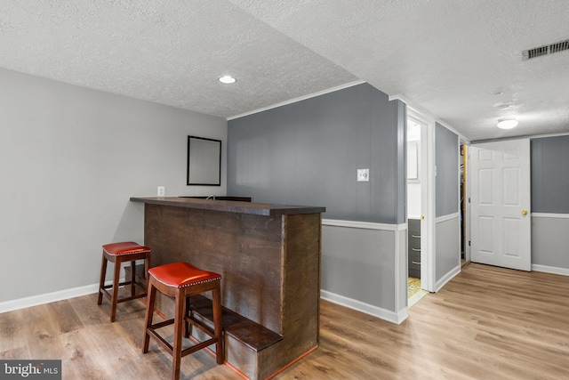 bar with visible vents, baseboards, a dry bar, wood finished floors, and a textured ceiling