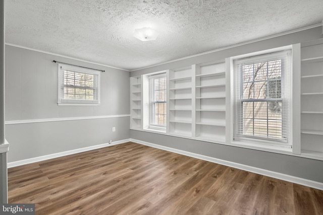 empty room featuring built in shelves, baseboards, ornamental molding, wood finished floors, and a textured ceiling