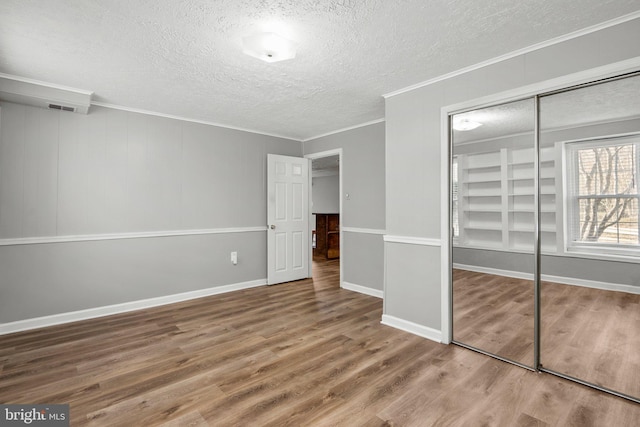 unfurnished bedroom with visible vents, crown molding, wood finished floors, a closet, and a textured ceiling