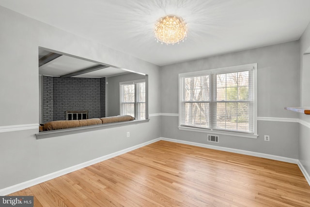 unfurnished living room with wood finished floors, visible vents, baseboards, a fireplace, and a notable chandelier