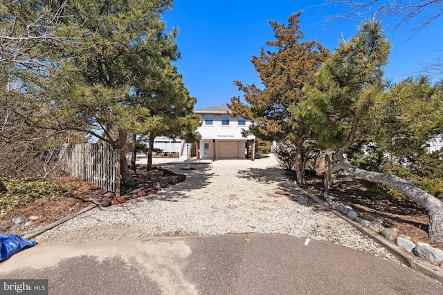 obstructed view of property with an attached garage, fence, and dirt driveway